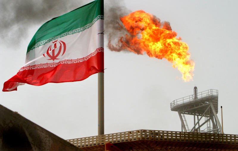 A gas flare on an oil production platform in the Soroush oil fields is seen alongside an Iranian flag in the Persian Gulf, Iran, on July 25, 2005. (Photo: Reuters)