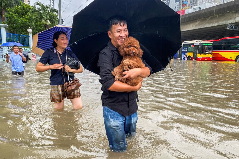 FILE PHOTO: A man carries a dog as he wades through a flooded street amid heavy downpours from Typhoon Matmo, which stranded vehicles, closed schools, moved classes online, and delayed flights to and from Noi Bai International Airport, in Hanoi, Vietnam, Oct 7, 2025. (Reuters)