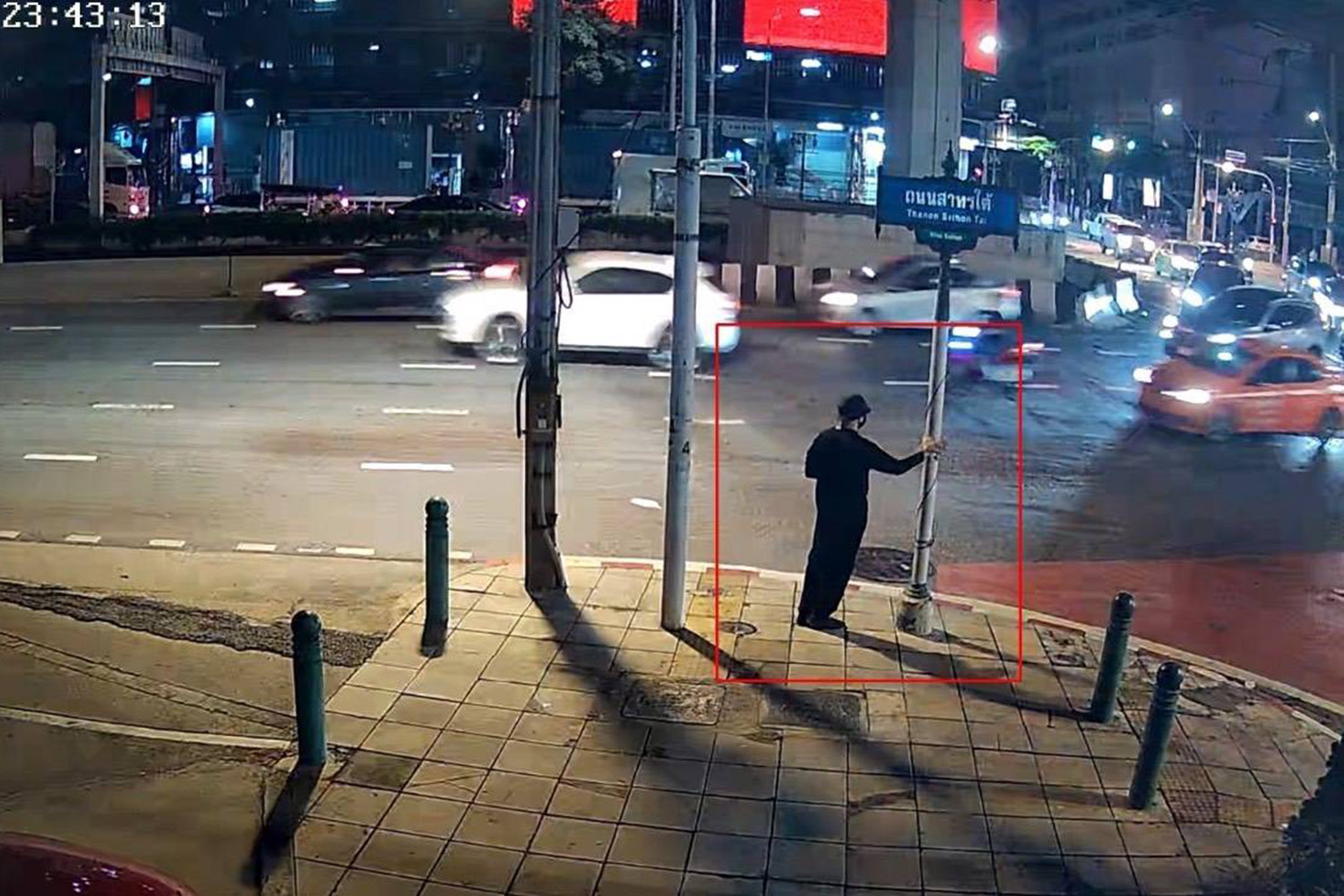 A still from surveillance recording shows a man applying a QR code sticker on a roadside pole at night in an area of Bangkok.