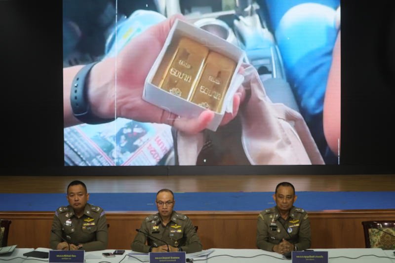A video of an exchange of gold bars plays behind senior officers as they discuss the case against former deputy chief Surachate Hakparn, at a briefing in Bangkok on Tuesday. (Photo: Pornprom Satrabhaya)