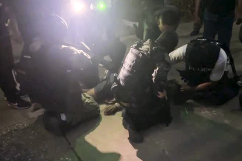 Police officers handcuff an 18-year-old gunman following a shooting and hostage-taking incident at Phatong Prathan Keeriwat School in Hat Yai on Wednesday evening. (Photo: Central Investigation Bureau)