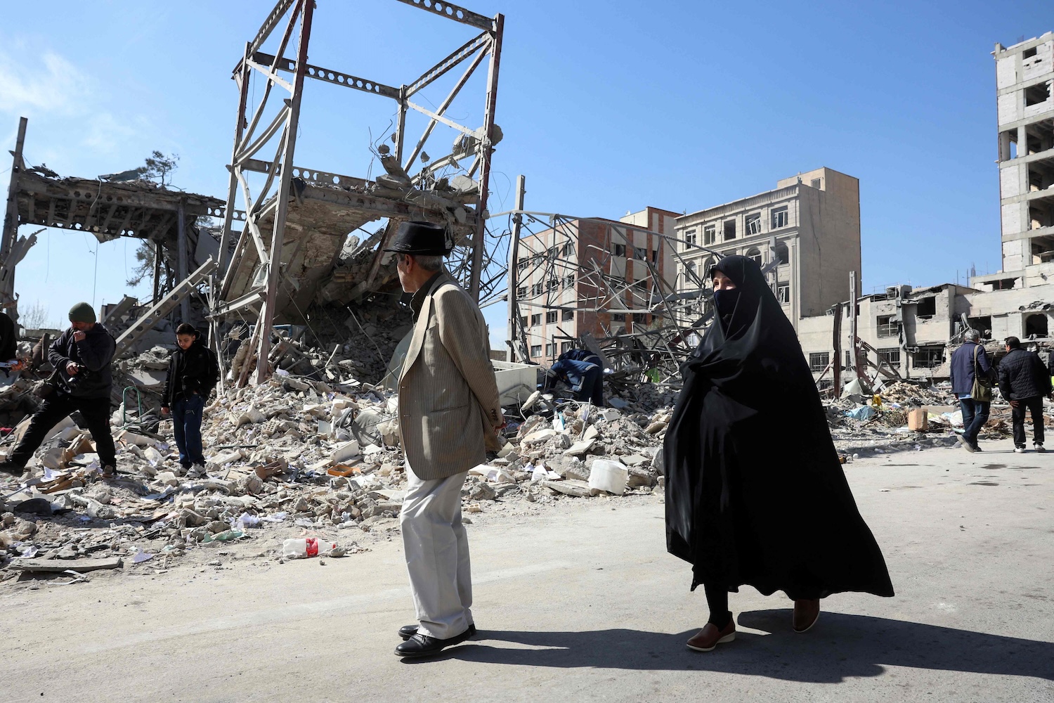 A man and a woman walk past destroyed buildings following aistrikes in central Tehran on March 4, 2026. (Photo: AFP)