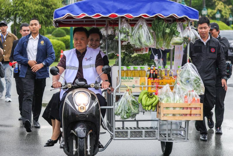 Prime Minister Anutin Charnvirakul and Deputy Prime Minister and Commerce Minister Suphajee Suthumpun ride on a mobile grocery tricycle to launch the "Thais Help Thais" campaign inside a compound of the Government House in Bangkok on Tuesday. (Photo: Reuters)