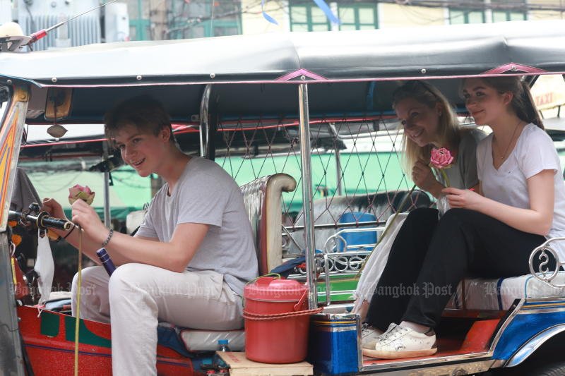 Tourists with lotus flowers in their hands pose as a tuk-tuk driver and passengers parked at Pak Klong Talat flower market in Bangkok on March 30. (Photo: Apichart Jinakul)