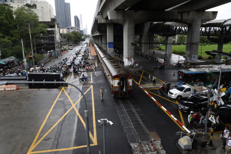 A railway-crossing official waves a green flag as a passenger train passes through the Asok-Phetchaburi railway crossing in Bangkok on May 20. (Photo: Nutthawat Wichieanbut)