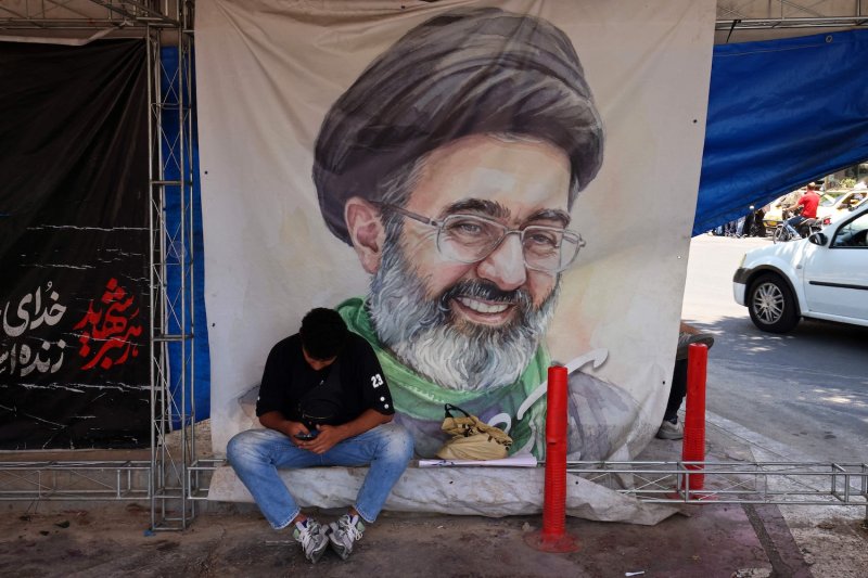 A man checks his phone in front of a poster with a portrait of Iranian supreme leader Mojtaba Khamenei, who has not been seen in public for nearly four months, at Vanak Square in Tehran on June 10, 2026. (Photo: AFP)