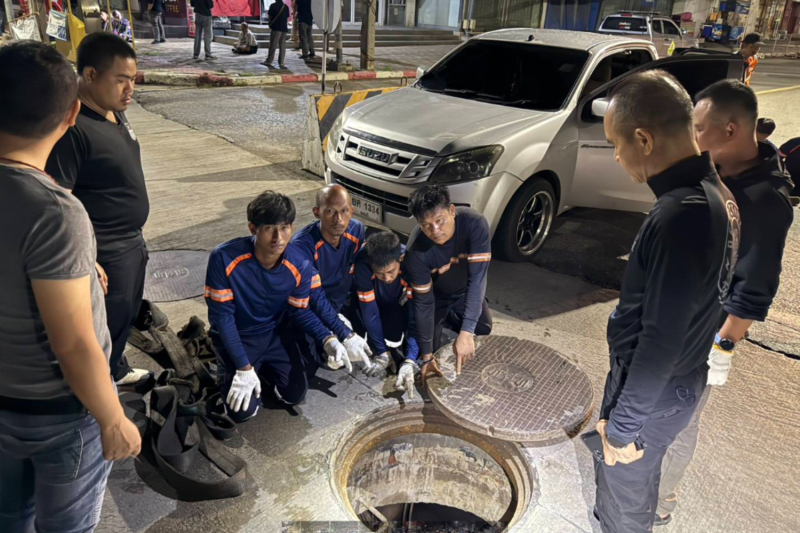 Some of the 18 arrested suspects — attired in custom-made uniforms bearing the name of a fake telecom company — show a manhole they opened in an attempt to steal underground copper cables in Muang district of Nakhon Sawan on Thursday. (Photo: Chalit Phoomrueng)