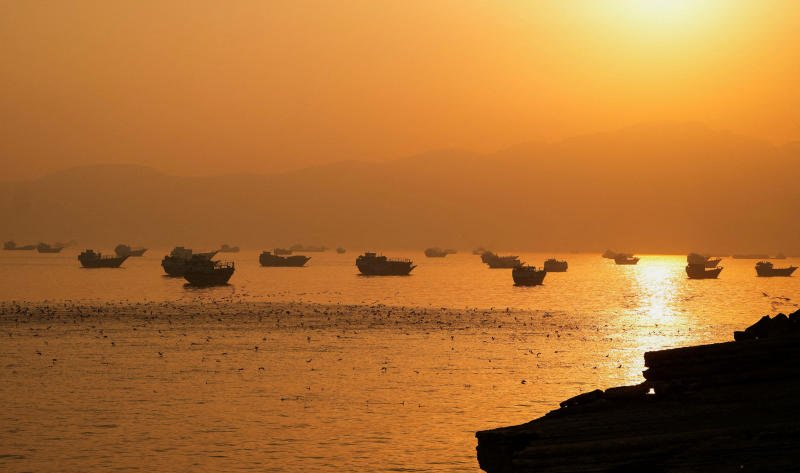Vessels halted in the blockaded Strait of Hormuz, bathed in the rising Sun, as seen from Oman. (photo: stringer/ Reuters)