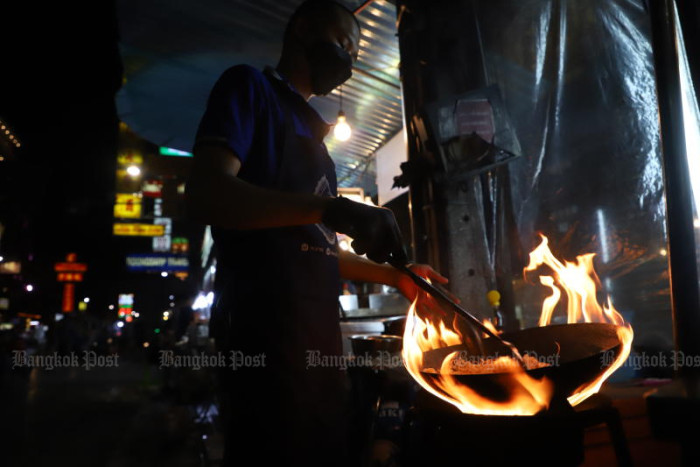 A person cooking over a large open fire at night.