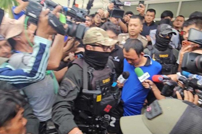A crowd of people, including media and law enforcement, gathered around a central figure.