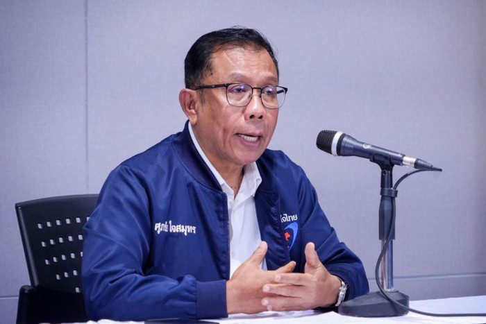 A man in a blue jacket speaking into a microphone at a table