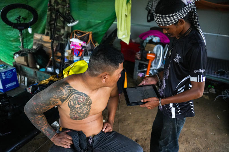 Tattoo artist Cheng Bora speaks with a customer at his house in Rong Cham, a resettlement site villagers have nicknamed "the waiting village", home to families who fled fighting along the Cambodia-Thailand border and are waiting for a chance to return, in Banteay Meanchey province, Cambodia, on Sept 15, 2026. (Photo: Reuters)