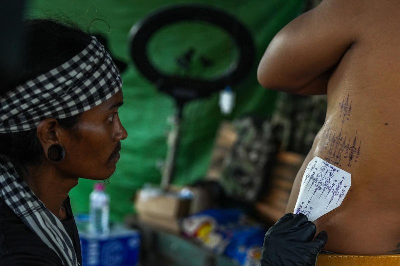 Tattoo artist Cheng Bora places the outlines of a talisman on a customer at his house in Rong Cham, a resettlement site villagers have nicknamed "the waiting village", home to families who fled fighting along the Cambodia-Thailand border and are waiting for a chance to return, in Banteay Meanchey province, Cambodia, on Sept 15, 2026. (Photo: Reuters)