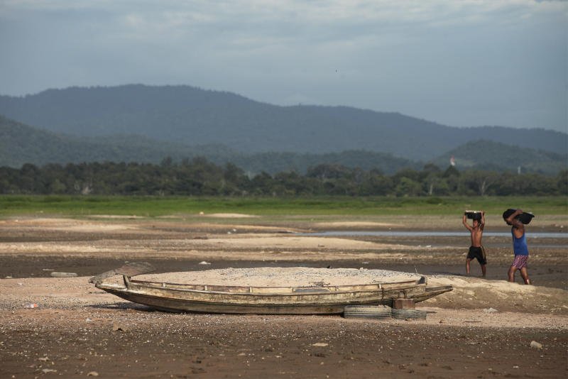 Villagers walk past an abandoned boat in a dried-up reservoir in Chon Buri province, Thailand. (Bangkok Post file photo)
