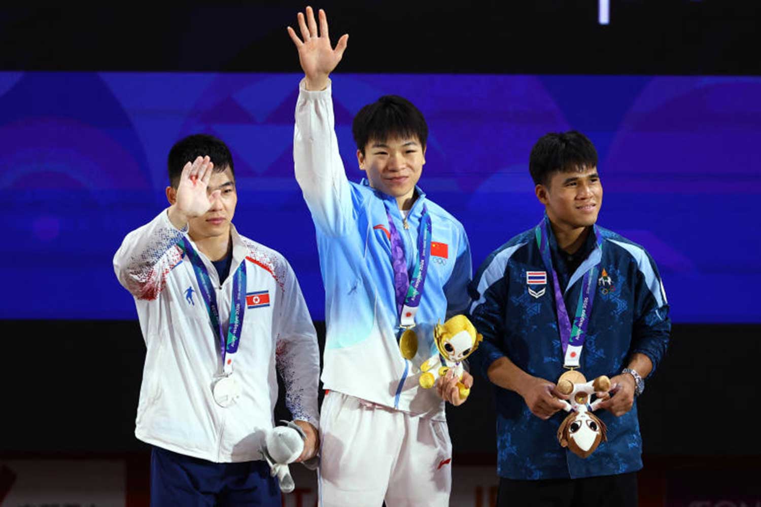 Asian Games - Aichi-Nagoya 2026 - Weightlifting - Nagoya City Trade and Industry Center, Nagoya, Japan - September 24, 2026 Gold medallist China's Yang Yang celebrates on the podium after winning the men's 60kg along with silver medallist North Korea's Pang Un Chol and bronze medallist Thailand's Theerapong Silachai. REUTERS