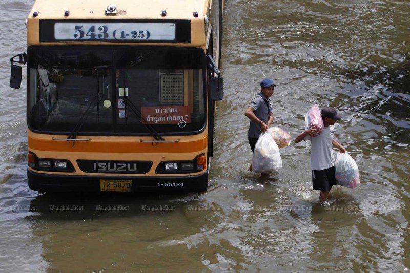 Residents get off a bus and wade through floodwater to return home after shopping along the busy Phahon Yothin Road in the northern Bangkok area on Tuesday. Pattarapong Chatpattarasill