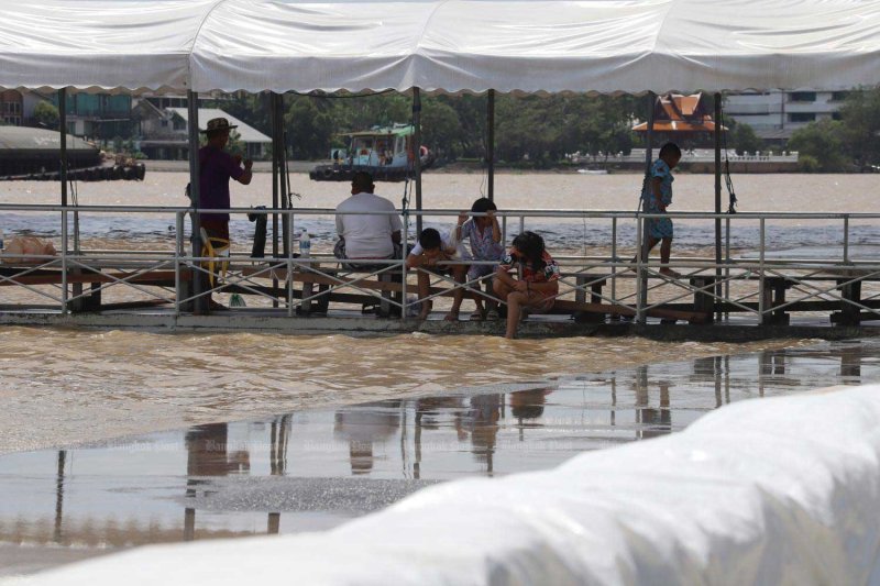 People sit at a pier near Rama VIII Bridge in Bangkok as the Chao Phraya River rises following the release of water at an average rate of 2,382 cubic metres per second. The level remains below Bangkok's flood-defence threshold of 3,600 cubic metres per second. photo: Apichart Jinakul