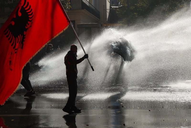 A protester holds an Albanian flag while being drenched by water cannon fired by police, in Tirana, Albania on Oct 17, 2026. (Photo: Reuters)