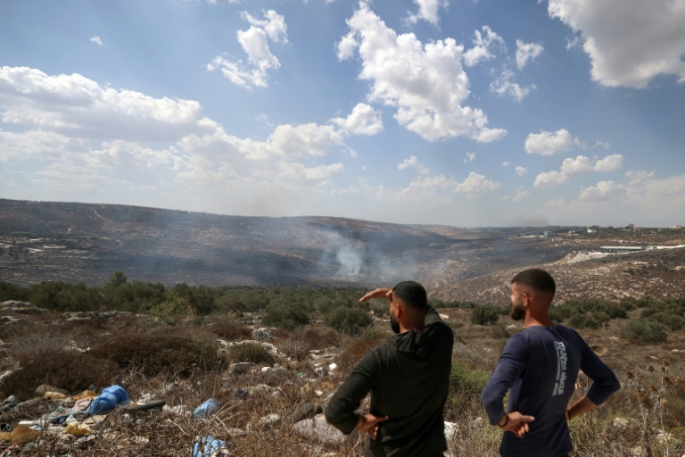 Palestinians stand on a hilltop looking down at the smoke from fires after Israeli soldiers fired tear gas at the olive harvest near the village of Asira al-Qibliya on October 3, 2026