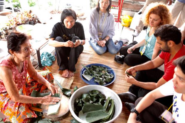 Grandma Berm teaches visitors how to cook khanom kluay. She and her niece instruct visitors on how to mix rice flour, sugar, salt, coconut shreds and ripe banana and steam the dessert. The cooking class lasts about two hours and everyone can taste their dessert while it is still hot. KARNJANA KARNJANATAWE