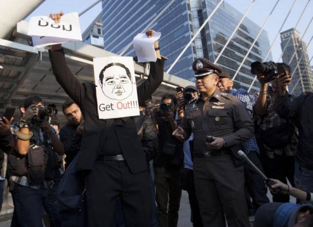 A member of the Young People for Social Democracy Movement attaches a photo of Deputy Prime Minister Prawit Wongsuwon to his face during a performance to pressure him to resign at Sathon-Narathiwat intersection in Bangkok yesterday. Pawat Laopaisarntaksin