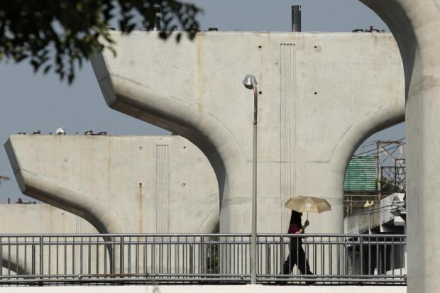 A woman walks past a construction site of the Green Line, one of several public transport projects likely to affect economic growth. (Photo by Patipat Janthong) A woman walks past a construction site of the Green Line, one of several public transport projects likely to affect economic growth. (Photo by Patipat Janthong)