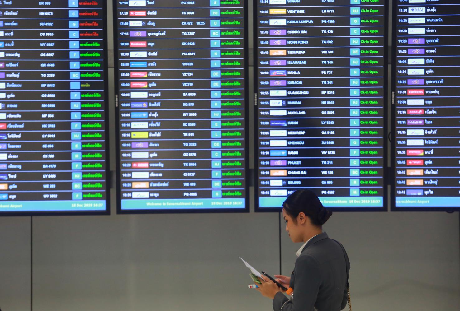 A woman stands at a display of flight information at Suvarnabhumi airport. South Korean airlines have suspended more flights to Thailand.