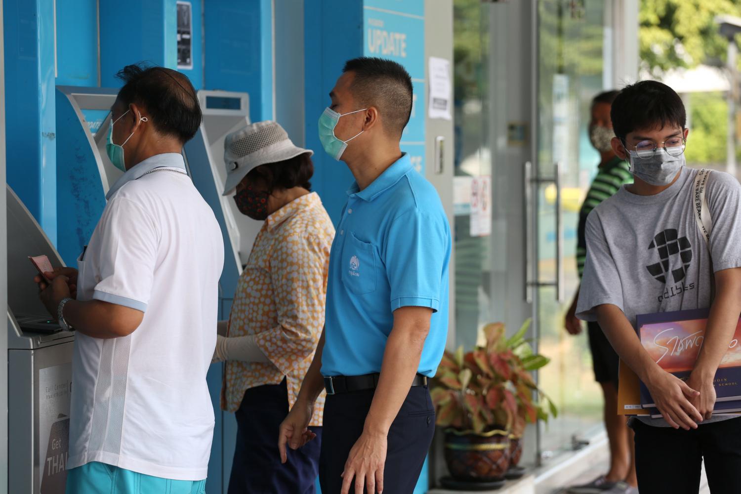 Customers queue at a Krungthai Bank ATM on Nawamin Road to receive a cash handout offered by the government. The Social Security Office expects to start issuing 5,000-baht monthly handouts within 10 days.