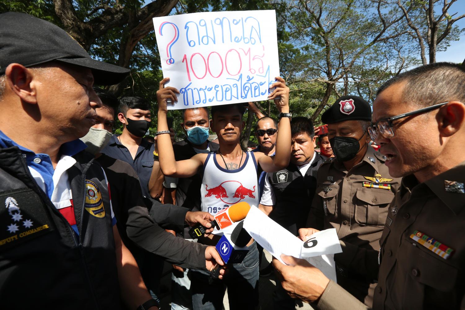 Activist Panupong Jadnok yesterday holds up a poster saying '1,000-rai sea reclamation. What will Rayong people get?' during Prime Minister Chan-o-cha's visit to a market ahead of Tuesday's mobile cabinet meeting. (Photo by Pattarapong chatpattarasill)