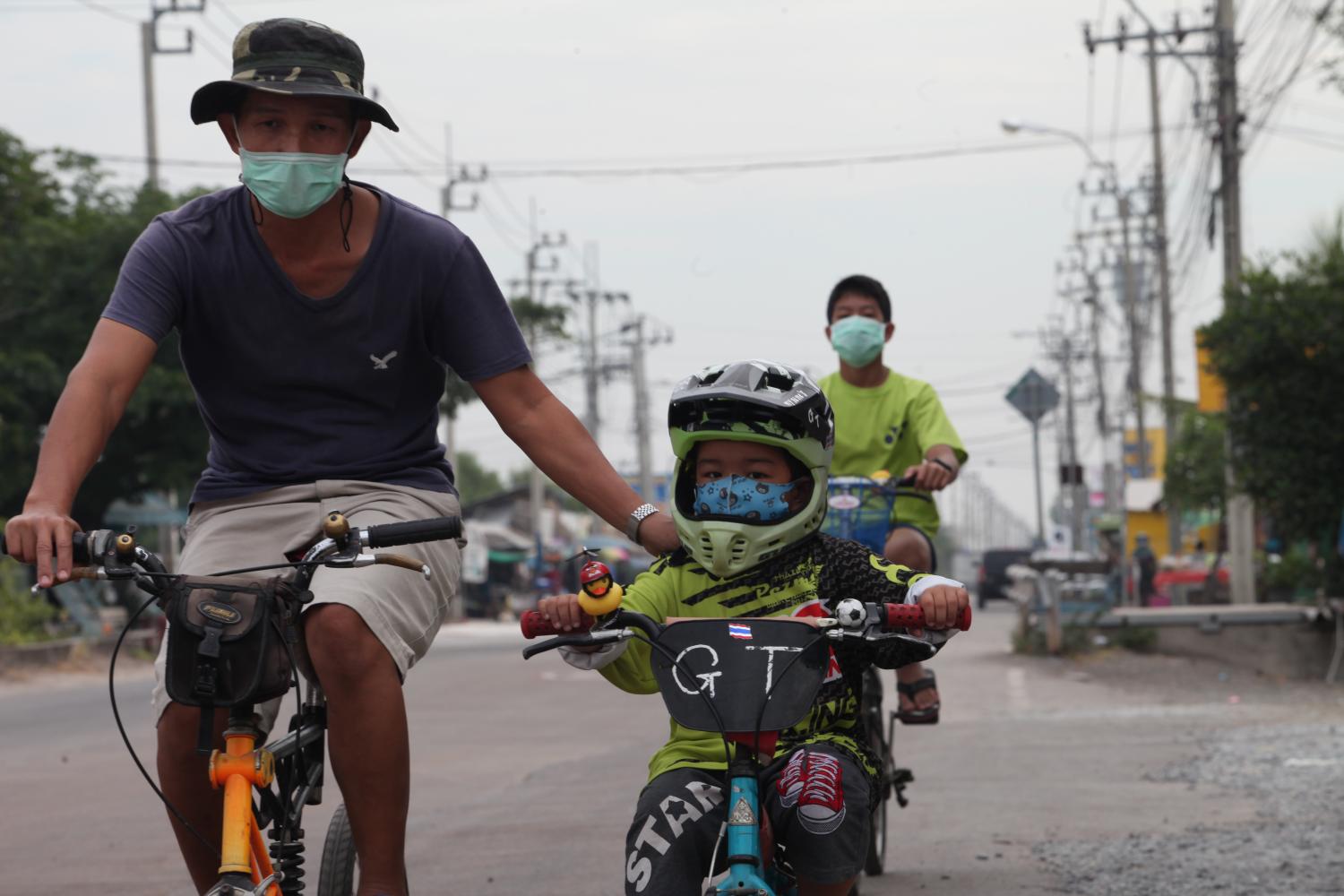 A man takes his son cycling in Bangkok's Bang Khunthian district. People are now wearing masks not only to protect themselves from Covid-19, but also fine dust pollution, which has spiked in parts of Bangkok. (Photo by Apichart Jinakul)