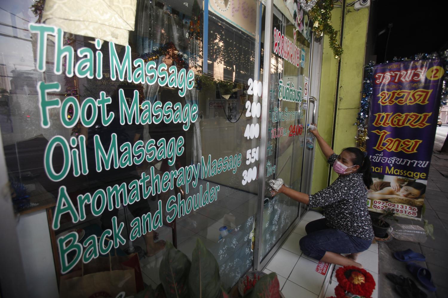 Ready for business: A woman cleans the front window of her traditional Thai massage shop in the Inthamara area of Bangkok as the business reopens.