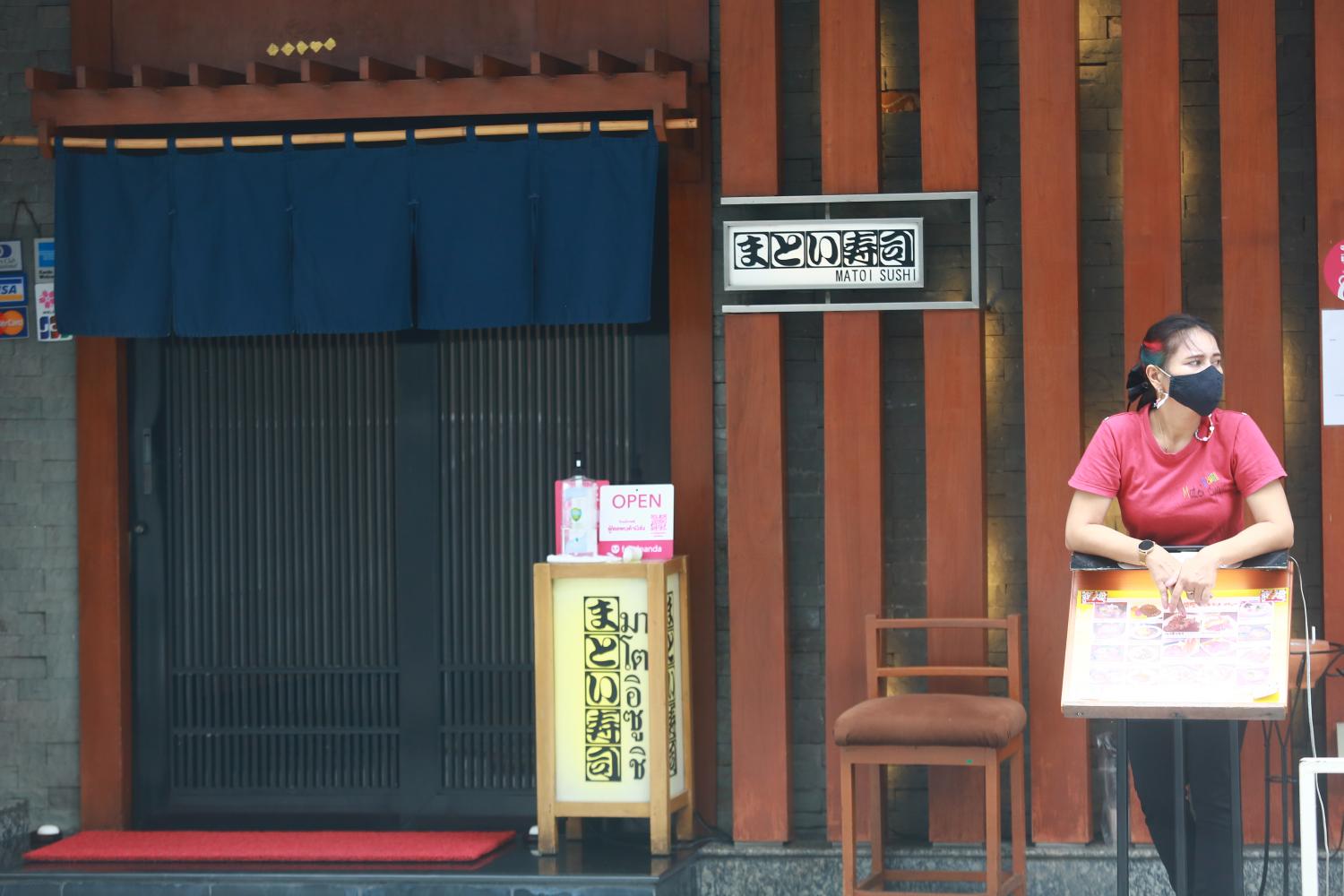 A worker at a Japanese restaurant in Bangkok's Silom area waits outside to greet customers.