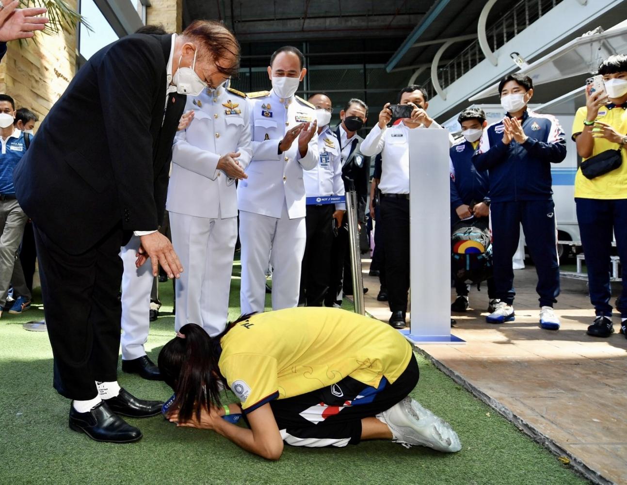 Olympic gold medallist Panipak Wongpattanakit prostrates in front of her father in Phuket as she arrives home following her win in Tokyo. Left  Panipak shows off her gold medal as she waves from a Phuket bus.  Photos by Phuket public relations office