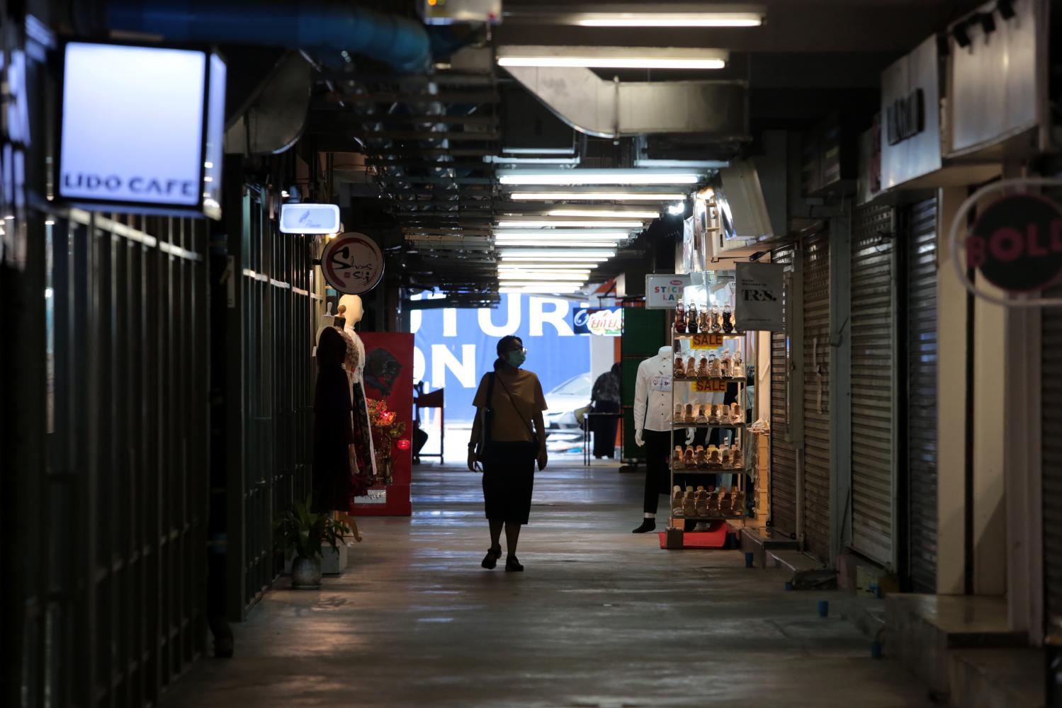 A woman looks at closed stores while walking alone in Siam Square in Pathumwan district. (Photo: Chanat Katanyu)