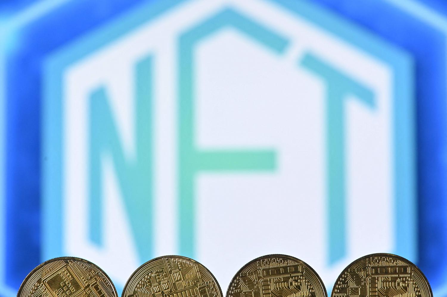 An illustration taken in London on Dec 30, 2021, shows gold-plated souvenir cryptocurrency coins arranged by a screen displaying an NFT logo. (AFP photo)