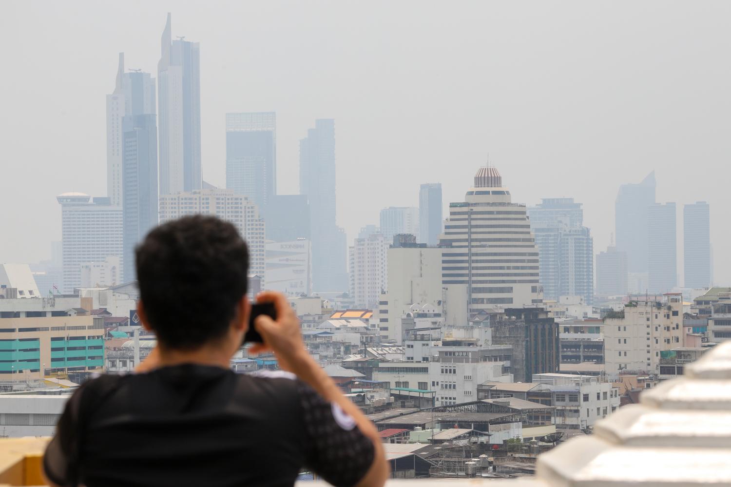 A visitor at Sa Ket temple takes a shot of the obscured Bangkok skyline from the top of the Golden Mount. Haze blanketed parts of the city yesterday, prompting health warnings. Pattarapong Chatpattarasill