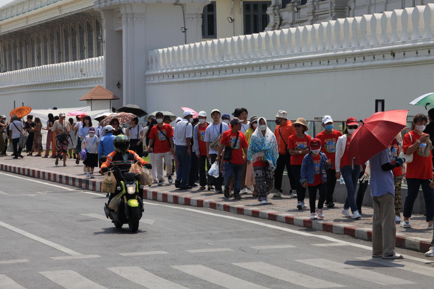 Tourists walk along a pavement next to the Temple of the Emerald Buddha, or Wat Phra Kaeo on Na Phra Lan Road, in the hot sunshine on Friday. (Photo: Apichart Jinakul)