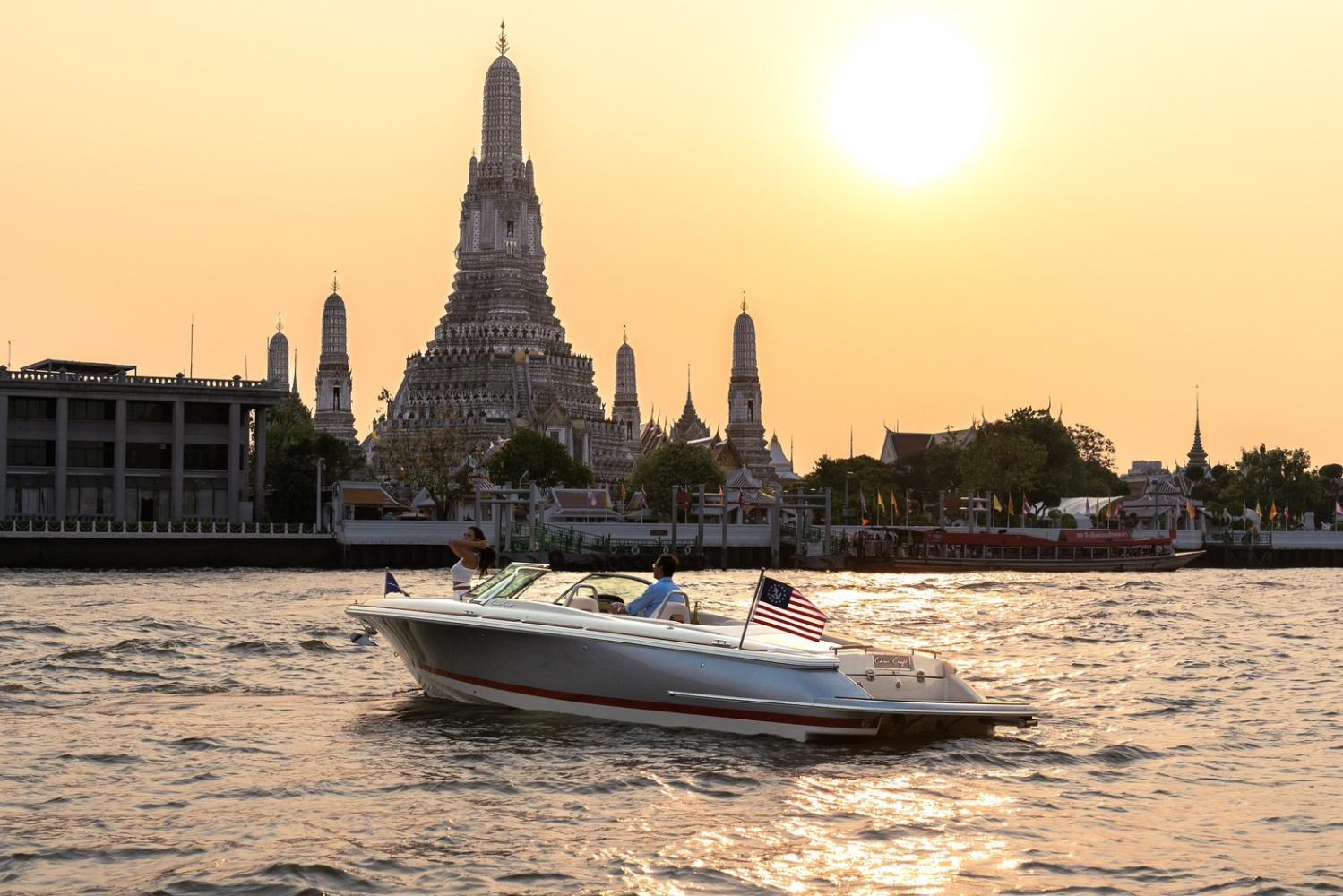 A Chris-Craft recreational boat cruises along the Chao Phraya River in Bangkok.